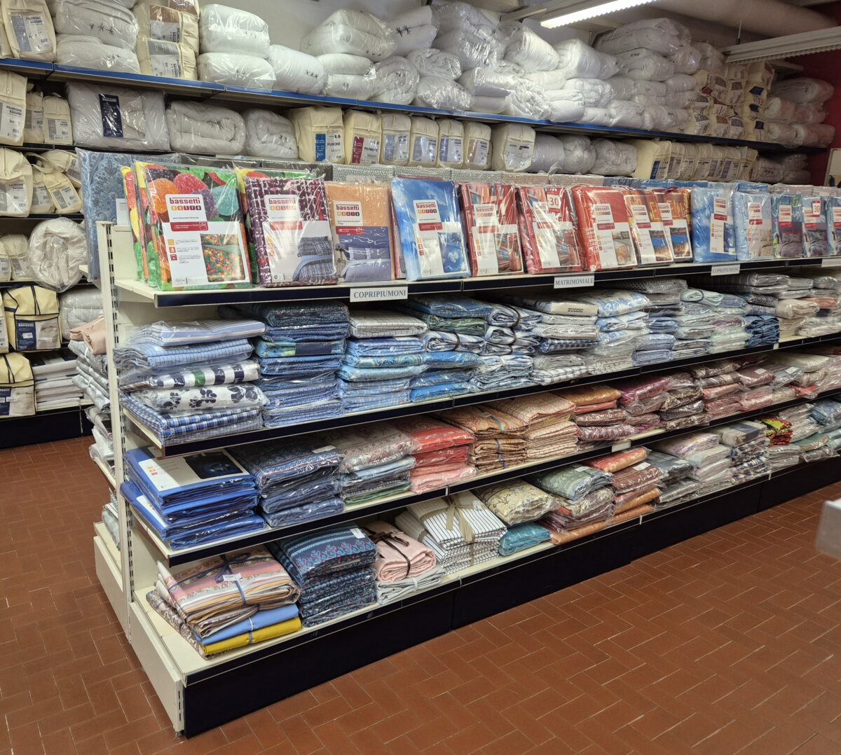 Innenraum eines Ladens, an den Wänden Regale mit eingepackten Decken, in der Mitte regale mit Bettwäsche